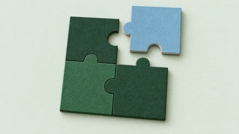 A blue paper puzzle piece fits into a green puzzle on a pale sage surface.